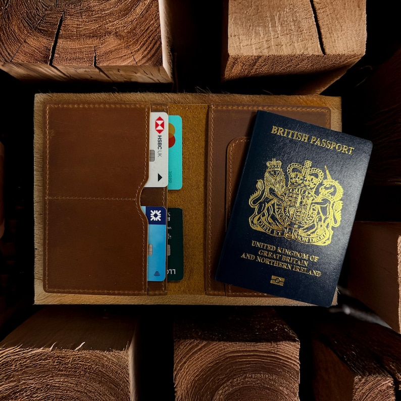 Pu&ograve; includere: Porta passaporto in pelle marrone aperto, con fessure per carte e un passaporto britannico. Il porta passaporto ha un bordo strutturato di colore chiaro. Le carte di credito sono visibili nelle fessure. Il passaporto &egrave; blu con scritte dorate.