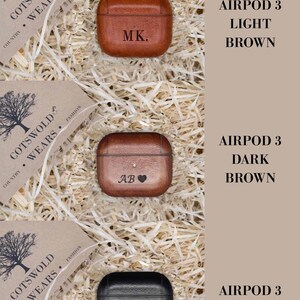 May include: Three Airpod 3 cases in different colors and materials. The first case is light brown leather with the initials "MK." engraved on it. The second case is dark brown leather with the initials "AB" and a heart engraved on it. The third case is black leather with the initials "NC" engraved on it.
