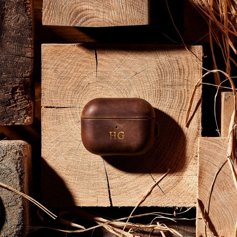 May include: A brown leather case for wireless earbuds with the initials "HG" embossed in gold on the front.