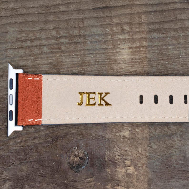 Pu&ograve; includere: Un cinturino per orologio con una sezione testurizzata color ruggine vicino al connettore in metallo argentato e una sezione in beige chiaro. La parte beige &egrave; impressa con le lettere dorate JEK e presenta quattro fori di regolazione.