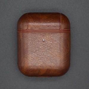 May include: A brown leather case for wireless earbuds. The case has a textured surface and a red trim around the edges.