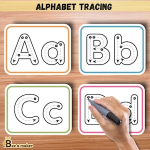 Könnte beinhalten: Vier weiße Karten mit schwarzen Umrissen und gepunkteten Linien zum Nachzeichnen der Buchstaben A, a, B, b, C, c und D, d. Die Karten befinden sich auf einem Holzmaserungshintergrund. Eine Hand zeichnet den Buchstaben D mit einem grauen Stift nach.