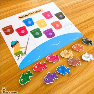May include: A colorful educational game for kids featuring a fishing theme. The game includes a sheet with buckets of different colors and fish of matching colors. The text on the sheet reads "Match the Colors".