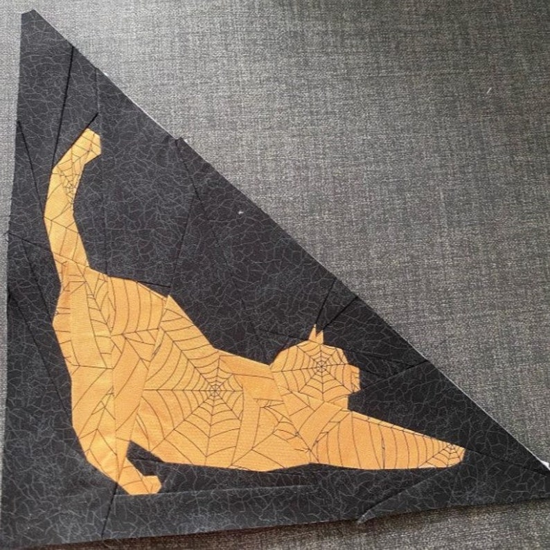 May include: A black fabric triangle with a yellow cat silhouette with a spiderweb pattern. The cat is in a stretched out pose with its tail in the air.
