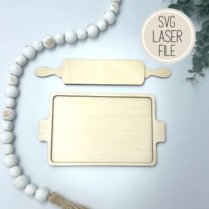 May include: A wooden tray with a handle on each side and a wooden rolling pin. The tray and rolling pin are both unfinished and ready to be painted or stained.