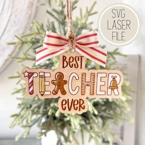 Può includere: Ornamento in legno con le parole "Best Teacher Ever" ed elementi decorativi come una matita, un omino di pan di zenzero e un righello. L'ornamento è sormontato da un fiocco a righe rosse e bianche e da un gancio in spago. Il testo "SVG Laser File" è in un cerchio.