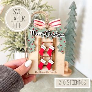 May include: Wooden Christmas ornament with a ladder design, red stockings, and the names Thomas, Kennedy, Rylie, and Emma. The ornament has a red and white striped bow and the words "Merry Christmas". The text "The Reynolds Family" is also included.