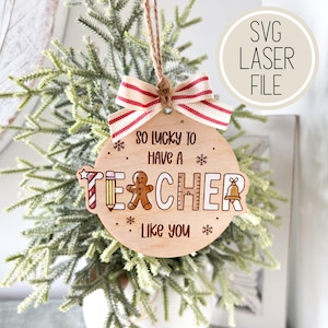 May include: A wooden disc-shaped ornament with the text "SO LUCKY TO HAVE A TEACHER LIKE YOU." It features a red and white striped bow and a hanging string. The word TEACHER is decorated with a pencil, gingerbread man, and bell.