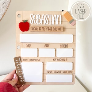 以下が含まれることがあります： 「Sebastian」という白い文字、赤いリンゴ、鉛筆が描かれた木製の初登校日用ボード。日付、年齢、身長、好きなもの、先生、将来の夢を記入する白い長方形のスペースがあり、側面に25cmの定規が取り付けられています。