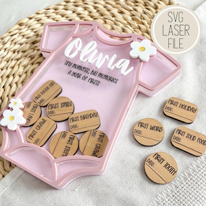 Puede incluir: Una caja de sombra rosa con forma de body con el nombre "Olivia" en escritura blanca. El texto "Tiny moments, big memories, a year of firsts" est&aacute; debajo. Incluye fichas de madera para registrar los hitos del beb&eacute;. El texto "SVG Laser File" est&aacute; en la parte superior derecha.