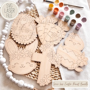 May include: A collection of unfinished wooden Easter-themed cutouts, including an egg, carrot, bunny, cross, and chick. The cutouts are decorated with floral designs and are accompanied by small paint pots and a paintbrush. The text "SVG LASER FILE" and "Score line Easter Paint Bundle" are visible.