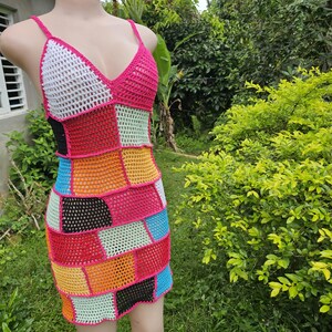 Pode incluir: Um vestido de crochê patchwork multicolorido com decote em V e alças finas. O vestido apresenta uma mistura de cores vibrantes, incluindo rosa, branco, preto, vermelho, amarelo, laranja, azul e verde. O vestido é exibido em um manequim.