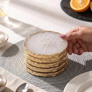 Hand stacking round natural white agate crystal coasters with gilded gold rim on dining table placemat