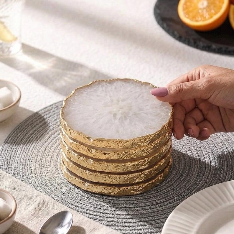 Hand stacking round natural white agate crystal coasters with gilded gold rim on dining table placemat
