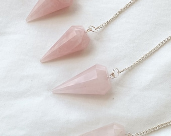 Puede incluir: Cuatro péndulos de cristal de cuarzo rosa con cadenas plateadas. Los péndulos son todos de la misma forma y tamaño, y están colgados de las cadenas.