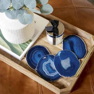 May include: Four blue agate coasters with a silver candle with a black ribbon on a wooden tray.