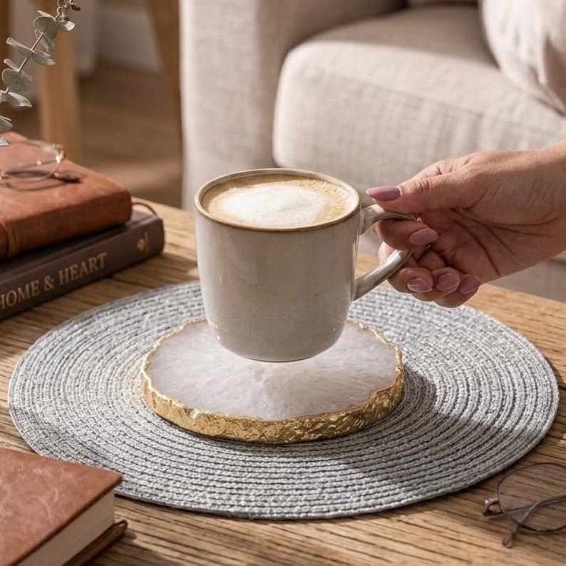 Person placing ceramic coffee mug on natural white agate crystal coaster with gold edge on wooden table