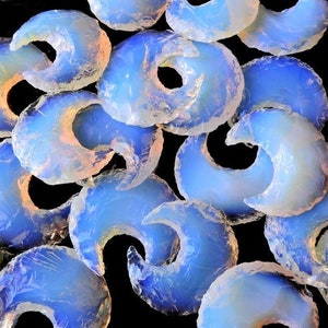 Pode incluir: Uma coleção de pedras em forma de lua crescente de cor azul iridescente e branca. As pedras são lisas e polidas, com uma aparência translúcida.