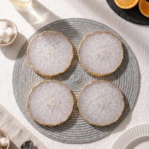 Set of 4 natural white agate slice drink coasters with gold trim arranged on grey placemat