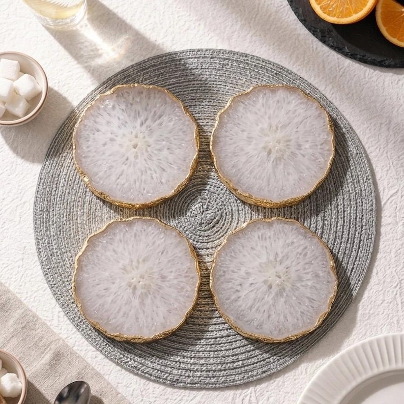 Set of 4 natural white agate slice drink coasters with gold trim arranged on grey placemat