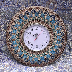 May include: A round, decorative wall clock with a white face and black Roman numeral hour markers. The clock is surrounded by a colorful, intricate design of blue, green, and gold.