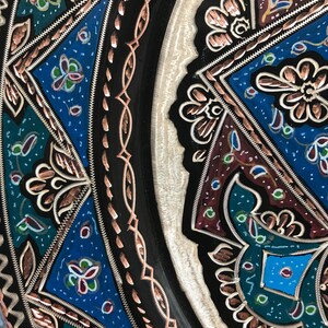 May include: A round metal plate with intricate copper and enamel designs. The plate features a black background with blue, green, and red floral patterns.