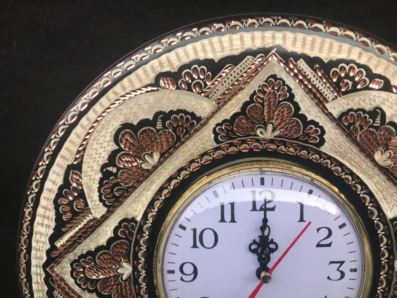 May include: A round, black and white clock with copper accents and intricate floral designs. The clock face is white with black numbers and hands.