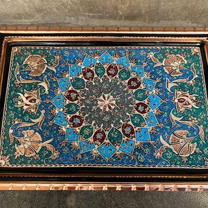 Puede incluir: Una bandeja de cobre decorativa con interior negro y diseños florales y geométricos intrincados en tonos de azul, verde, dorado y rojo.
