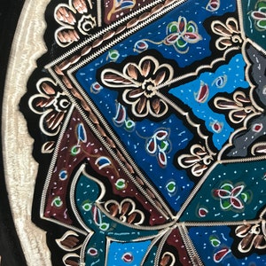 May include: A black metal tray with a decorative design featuring intricate copper and silver details. The design includes geometric shapes, floral patterns, and a variety of colors, including blue, green, red, and gold.