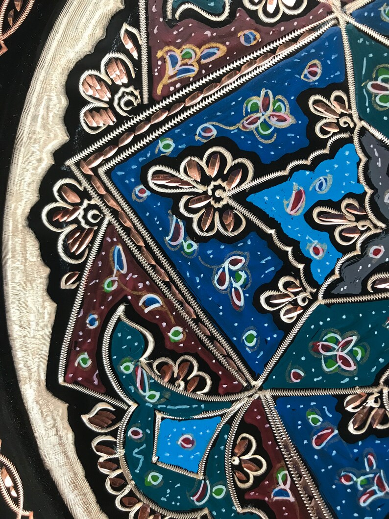 May include: A black metal tray with a decorative design featuring intricate copper and silver details. The design includes geometric shapes, floral patterns, and a variety of colors, including blue, green, red, and gold.