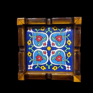 Könnte beinhalten: Quadratischer Aschenbecher aus Holz mit einem blauen Keramikflieseneinsatz. Die Fliese zeigt ein symmetrisches Blumenmuster mit roten Blüten, weißen Akzenten und gelben und grünen Details. Der Holzrahmen hat eine dunkelbraune Oberfläche.