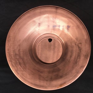 May include: A copper-coloured metal plate with a circular indentation in the centre. The plate has a smooth, slightly textured surface.