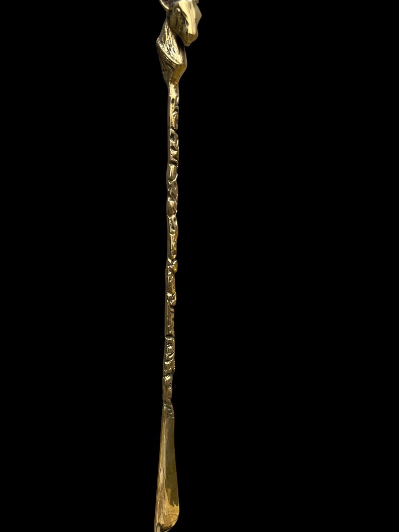 May include: A long, slender brass shoehorn featuring a detailed animal head handle at the top. The shaft of the shoehorn has a textured, organic surface, while the bottom end is smooth, polished, and curved to assist with sliding a foot into a shoe.