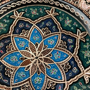 Puede incluir: Un plato decorativo con un dise&ntilde;o floral azul, verde y dorado. El plato est&aacute; hecho de metal y tiene un acabado brillante.
