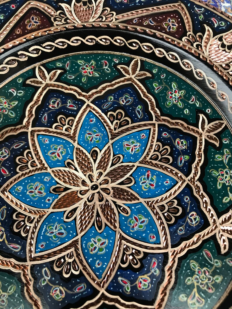 Puede incluir: Un plato decorativo con un dise&ntilde;o floral azul, verde y dorado. El plato est&aacute; hecho de metal y tiene un acabado brillante.