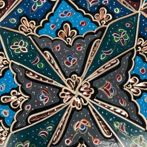 May include: A close-up of a decorative object with a black background and intricate gold and copper designs. The object is painted with blue, green, red, and white colors.
