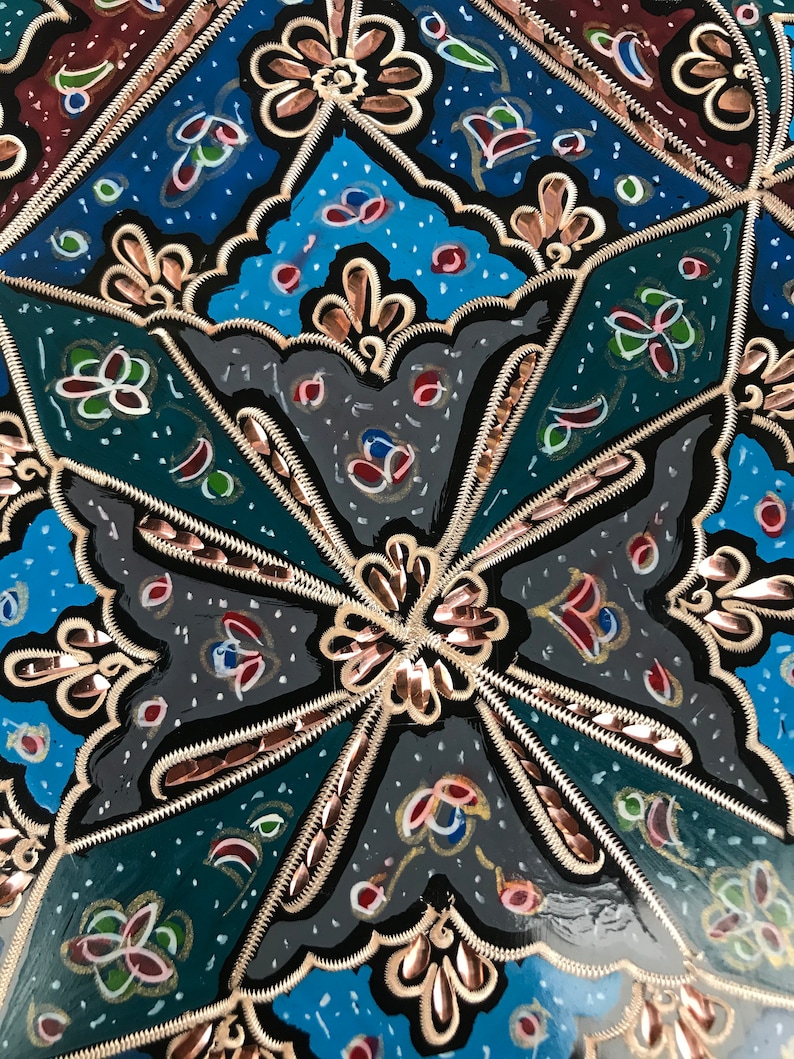 May include: A close-up of a decorative object with a black background and intricate gold and copper designs. The object is painted with blue, green, red, and white colors.