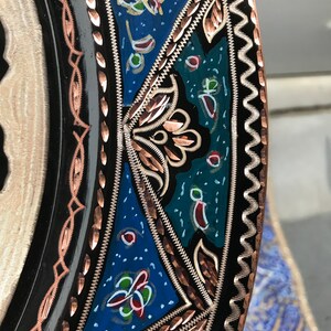 May include: Close-up of a decorative plate with a black background and intricate copper and silver designs. The plate features a blue, green, and red floral pattern.