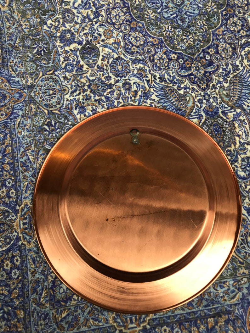 May include: A large, round copper plate with a slightly raised rim. The plate has a smooth, shiny surface and is free of any visible markings or designs.