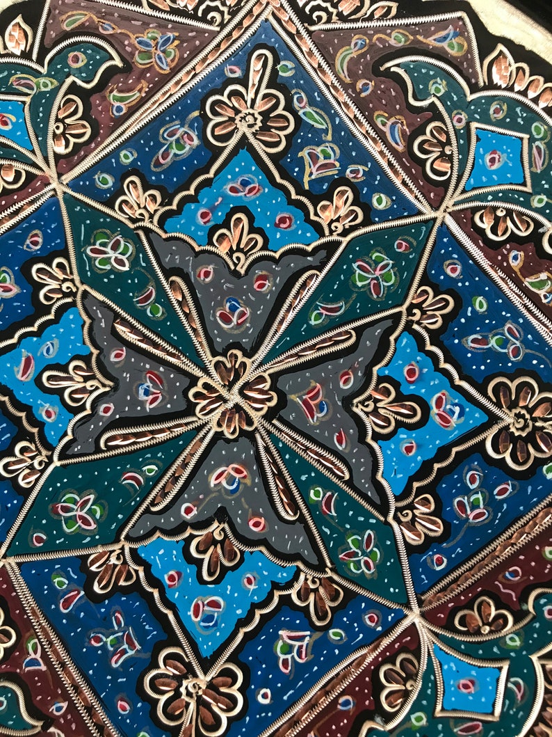 May include: A decorative metal tray with a geometric pattern in shades of blue, green, red, and gold. The tray has a black background and intricate details.