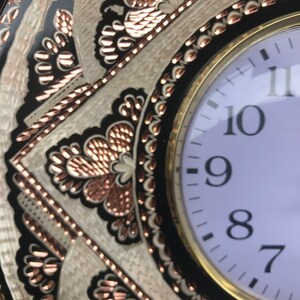 May include: A round, black and white clock with copper accents. The clock face is white with black numbers and hands. The clock is surrounded by a decorative border with a copper and white design. The clock says "quartz" at the bottom.