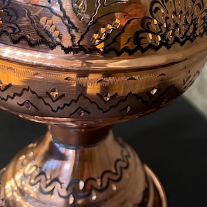 Op de afbeelding: Close-up van een koperen kom met gedetailleerde bloemen- en geometrische patronen. De kom heeft een voet en een brede, afgeronde body. De patronen zijn ge&euml;tst en geaccentueerd met zwart.