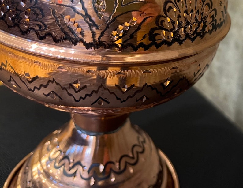 Op de afbeelding: Close-up van een koperen kom met gedetailleerde bloemen- en geometrische patronen. De kom heeft een voet en een brede, afgeronde body. De patronen zijn ge&euml;tst en geaccentueerd met zwart.