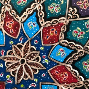 Puede incluir: Un plato de metal decorativo con un patr&oacute;n geom&eacute;trico en tonos de azul, rojo, verde y dorado. El plato tiene un dise&ntilde;o en relieve texturizado.