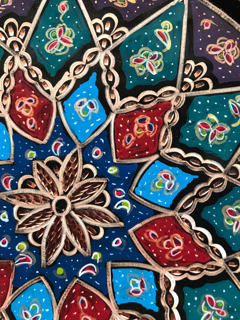 Puede incluir: Un plato de metal decorativo con un patr&oacute;n geom&eacute;trico en tonos de azul, rojo, verde y dorado. El plato tiene un dise&ntilde;o en relieve texturizado.