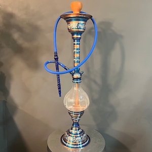 May include: A blue and gold hookah with a clear glass base and a blue hose. The hookah has intricate designs and is decorated with gold accents.