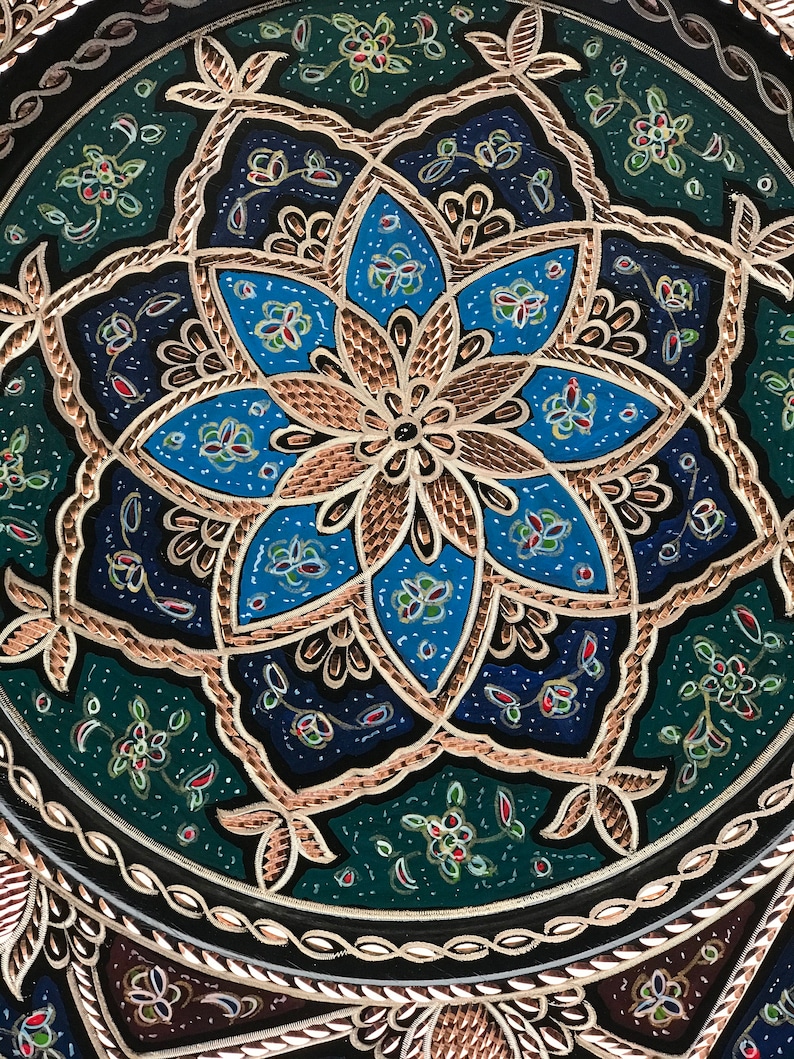 Puede incluir: Una bandeja redonda decorativa con un dise&ntilde;o floral de cobre y azul. La bandeja tiene un fondo negro con un borde de cobre.