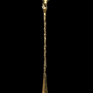 May include: A gold-colored metal shoehorn featuring a long, slender handle with an intricate, embossed floral pattern. The top of the handle is shaped like the head of an antelope with curved horns, while the bottom features a smooth, curved scoop.