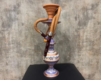 Pode incluir: Uma cachimba roxa e dourada com uma mangueira marrom. A cachimba tem desenhos intrincados e está sobre uma superfície preta.