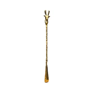 May include: A long, slender gold-colored metal shoehorn featuring a sculpted deer head handle at the top. The handle transitions into a textured, branch-like stem that leads down to a smooth, curved, and polished scoop at the bottom end.